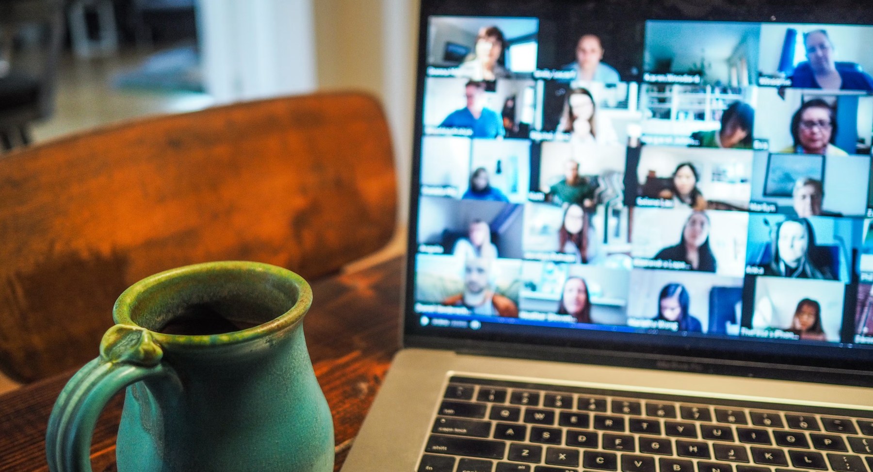 A laptop showing a grid of faces on a video call, a mug beside it