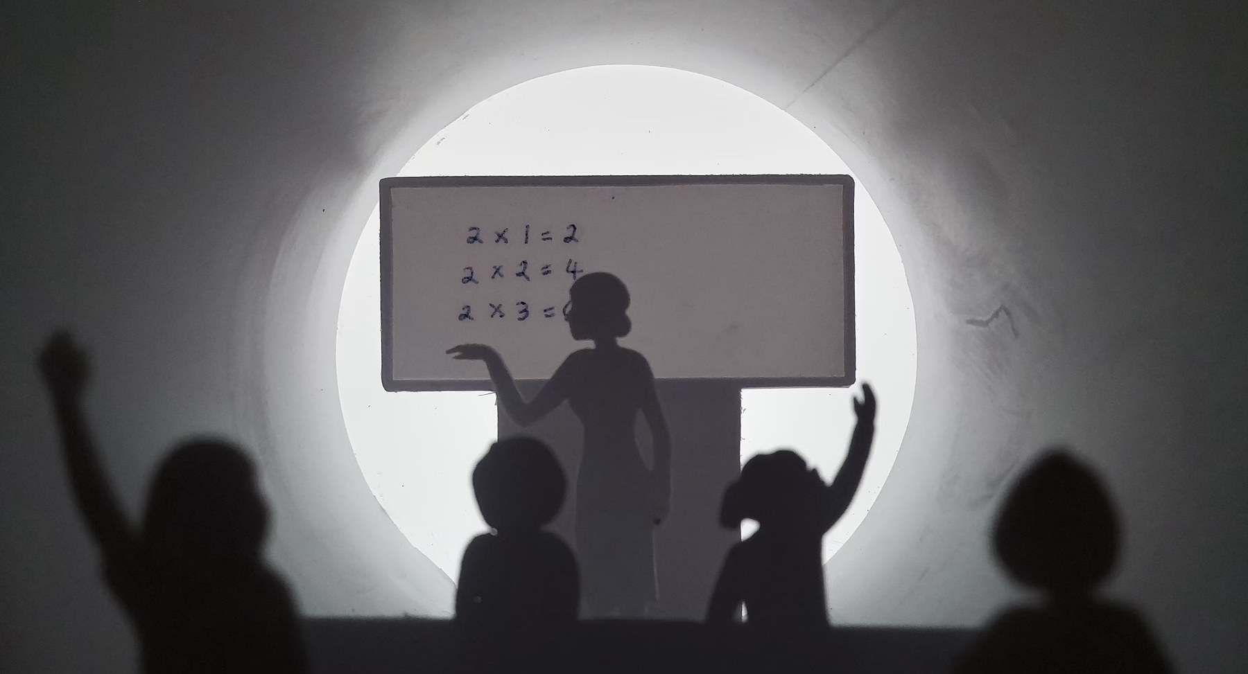 A shadow-puppet classroom scene, a teacher at the board with hands raised