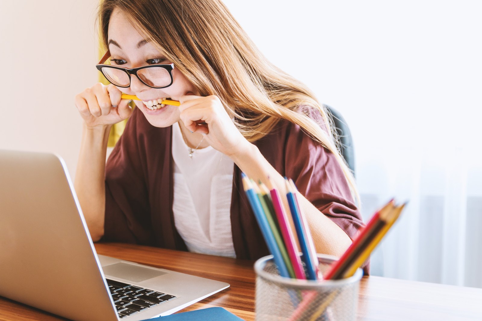 A student at a laptop biting a pencil, visibly stressed and overwhelmed