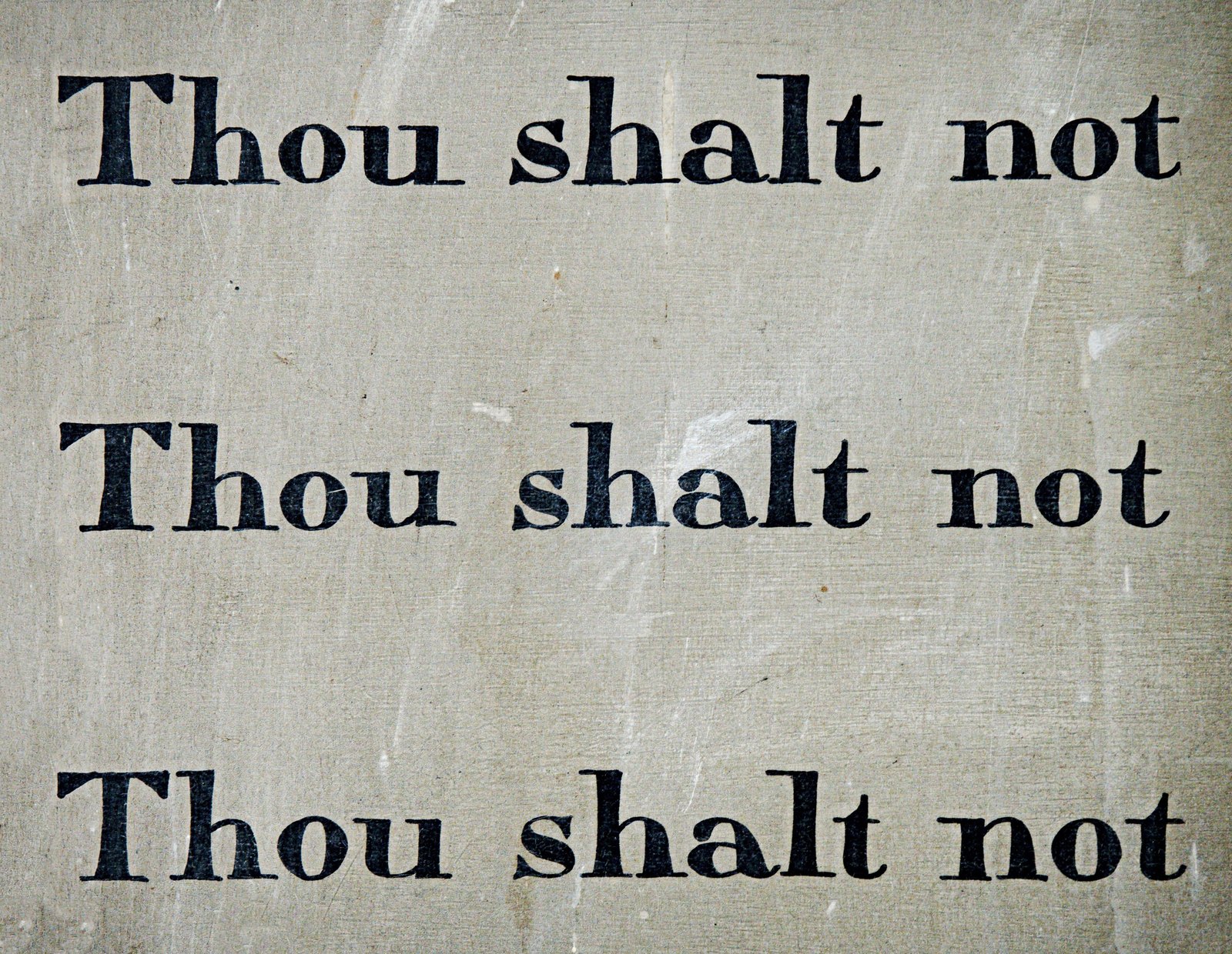 The words ‘Thou shalt not’ printed three times on a worn surface